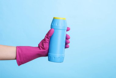 Mavi arka planda deterjan şişesi tutan mor kauçuk temizleme eldiveni. Ev temizliği ve temizlik konsepti