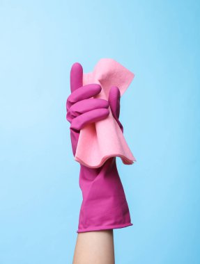 Mor kauçuk temizleme eldiveni mavi arka planda bez tutuyordu. Ev temizliği ve temizlik konsepti