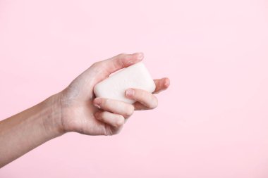 Kadının eli pembe arka planda köpüklü sabun tutuyor. Hijyen, temiz eller.