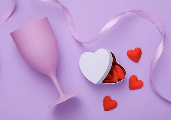 stock image Anniversary, holiday concept. Plastic glasse and a box with many hearts and a satin ribbon on a lavender background. Valentine's Day. Top view