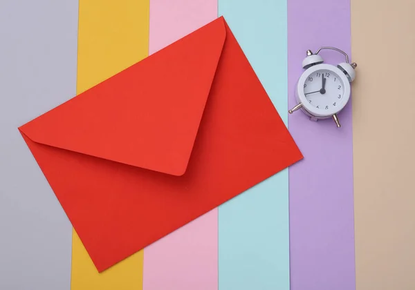 Renkli Arka Planda Alarm Saati Olan Kırmızı Bir Zarf Üst — Stok fotoğraf