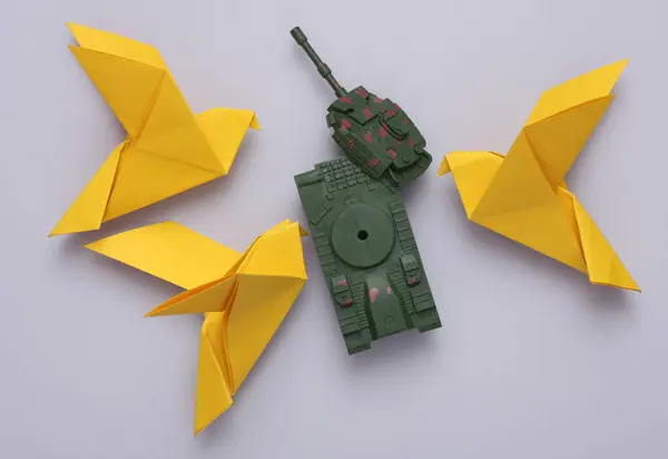 stock image Yellow origami doves and a broken military tank on gray background. Peace symbol, no war