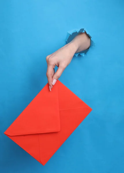 Frauenhand Hält Roten Umschlag Durch Zerrissenes Loch Blauem Papier — Stockfoto