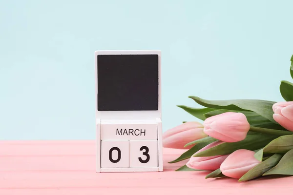 Block wooden calendar with the date March 03 and tulips on a pastel background. Spring composition