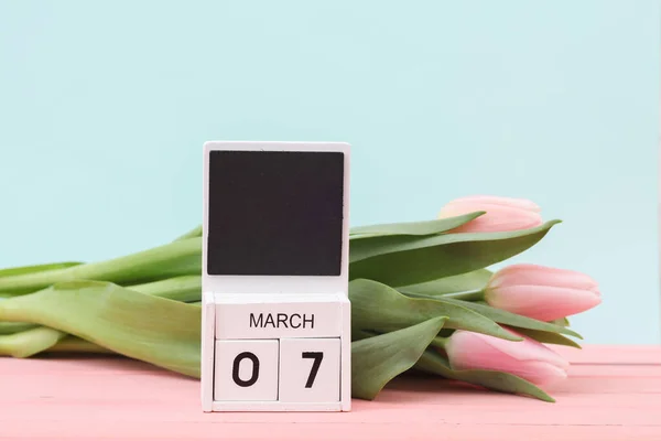 Block wooden calendar with the date March 07 and tulips on a pastel background. Spring composition