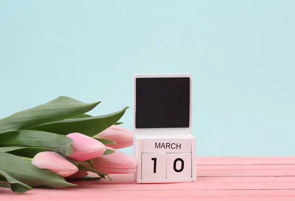 Block wooden calendar with the date March 10 and tulips on a pastel background. Spring composition