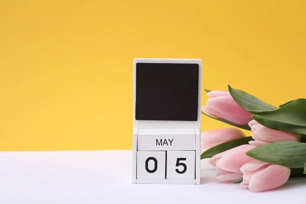 Stock image Block wooden calendar with the date may 05 and tulips on a yellow background. Spring composition