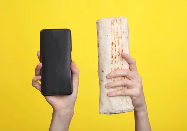 stock image Female hands holding shawarma and smartphone on a yellow background