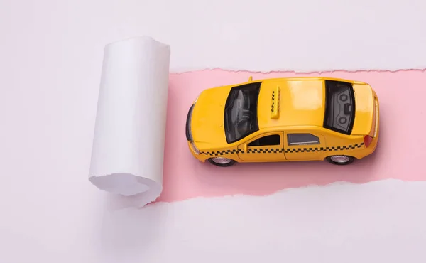 Toy taxi car on a pink background with torn paper.