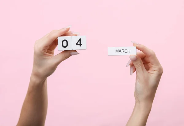 stock image Woman's hands hold wooden block calendar with the date 04 march on pink background