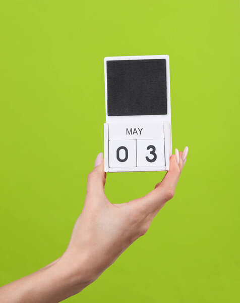 Блок календарь с датой 03 мая в женской руке на зеленом фоне