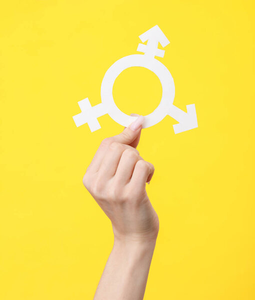 Female hand holding a transgender gender symbol on a yellow background