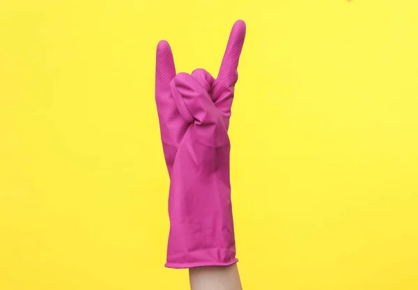 Stock image Hand in purple rubber cleaning glove shows rock symbol on a yellow background. House cleaning and housekeeping concept