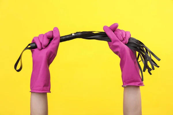 手拿着紫色橡胶清洁手套 手拿着黄色背景的性商店皮鞭 — 图库照片