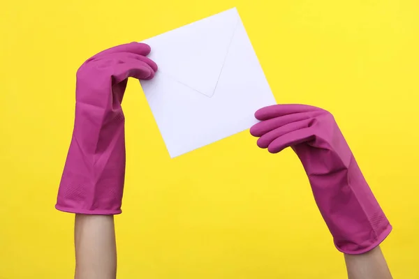 黄色の背景に白い封筒を保持紫色のゴムクリーニング手袋で手 清掃とハウスキーピングのコンセプト — ストック写真