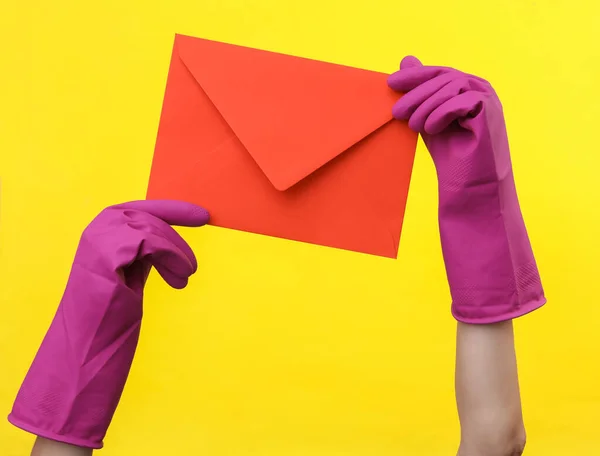 黄色の背景に赤い封筒を保持紫色のゴムクリーニング手袋で手 清掃とハウスキーピングのコンセプト — ストック写真