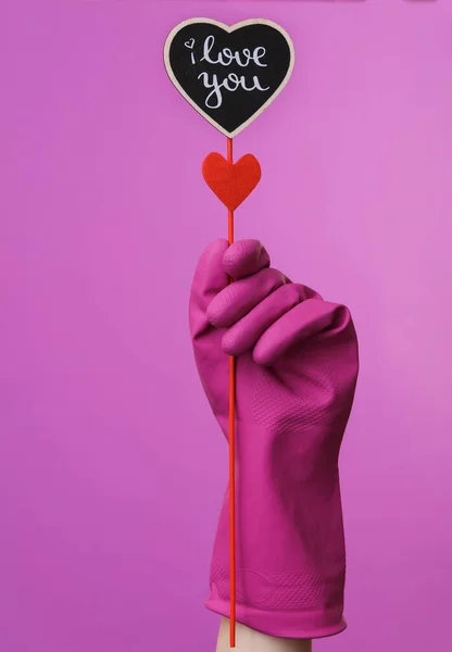 Hand in purple rubber cleaning glove holding valentine on purple background.