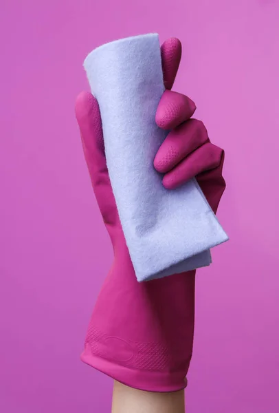 Hand in purple rubber cleaning glove holding rag on purple background. House cleaning and housekeeping concept