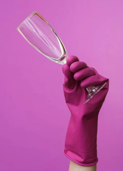 Hands in purple rubber cleaning gloves holding glass on a purple background.
