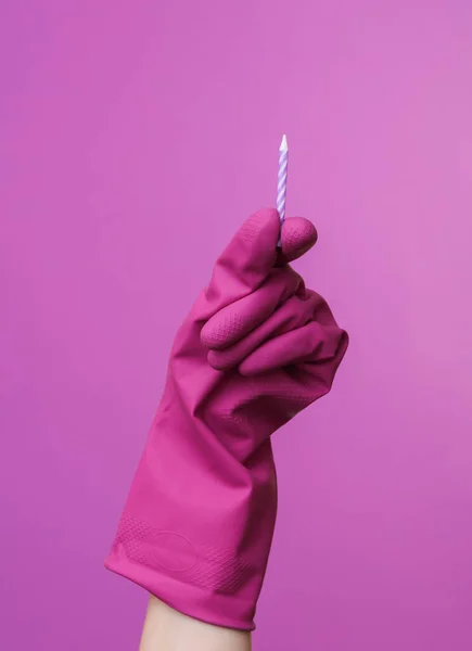 Hands in purple rubber cleaning gloves holding birthday candle on a purple background.