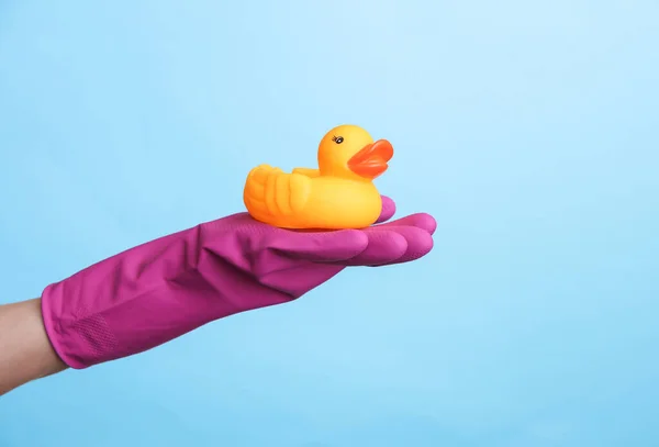 stock image Hand in purple rubber cleaning glove holding rubber duck on a blue background. House cleaning and housekeeping concept