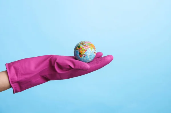 Hand in purple rubber cleaning glove holding globe on blue background. House cleaning and housekeeping concept