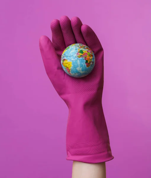 紫色の背景に地球を保持紫色のゴムクリーニング手袋で手 清掃とハウスキーピングのコンセプト ロイヤリティフリーのストック画像