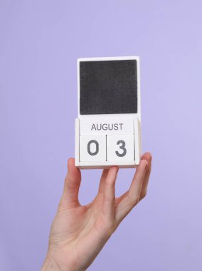 Kadının elinde ahşap takvim var. Tarih Ağustos 03. Pastel mor arka plan.