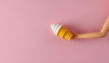 Doll 'un eli pembe arka planda dondurmayı tutuyor. Yaratıcı yerleşim