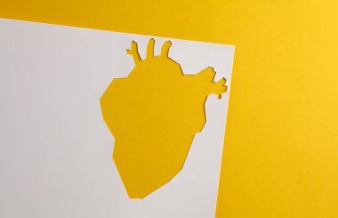 Sarı arka planda anatomik kalp şeklinde bir kağıt deliği. Kalp sağlığı konsepti