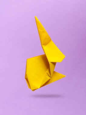 Sarı origami tavşanı mor arka planda uçuyor.
