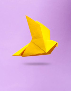 Sarı origami güvercini mor arkaplanda uçuyor
