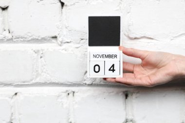 Kadınların elinde tahta bloklama takvimi var. Tarih Kasım 04, tuğla duvar arkasında.