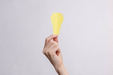 Beyaz bir arkaplanda kağıt kesiği ampulü tutan eller.