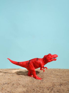 Mavi arka planda kumdaki Tyrannosaurus rex oyuncağı
