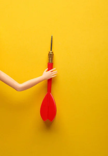 Puppet hand holding darts on yellow background