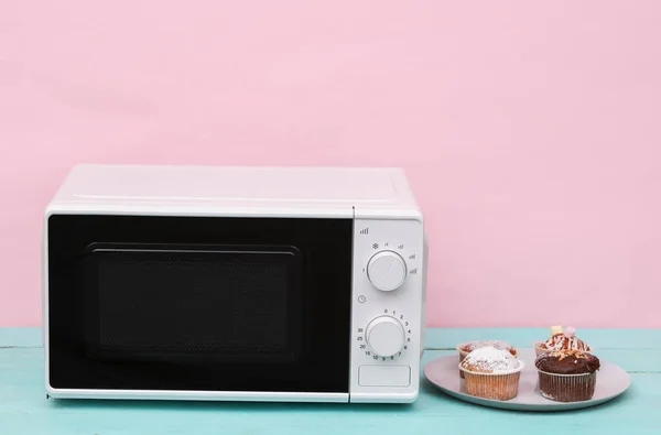 Modern microwave oven with cupcakes on a pastel background
