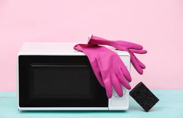 Microwave with cleaning gloves and a sponge on a pastel background. Cleaning in the kitchen concept