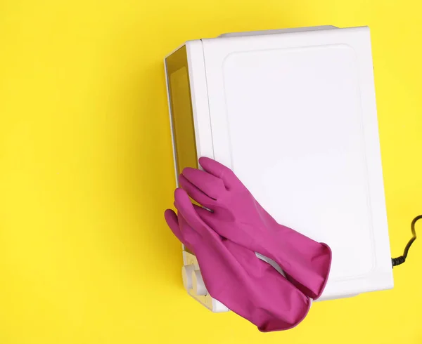 Microwave with cleaning gloves on yellow background.  Kitchen cleaning concept. Top view