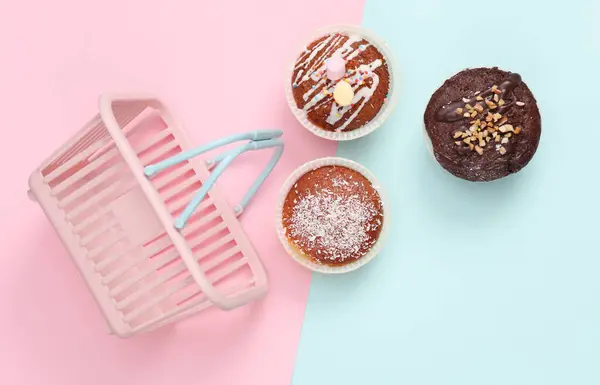 Supermarket basket and cupcakes on blue pink pastel background. Top view
