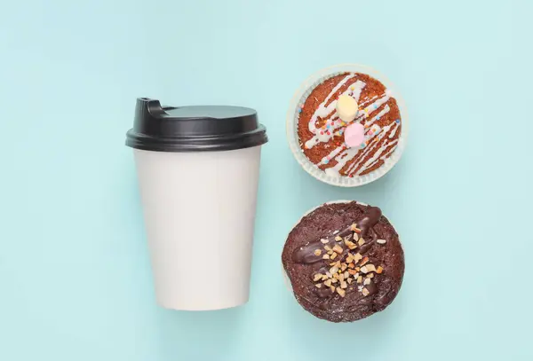 Takeaway coffee cup with cupcakes on blue background. Top view