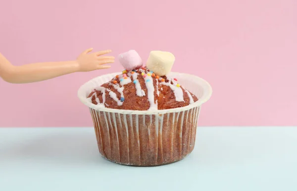 Appetizing muffin with puppet hand on blue-pink pastel background. Food concept