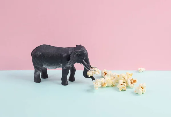 Toy elephant with popcorn on a blue-pink background. Creative layout