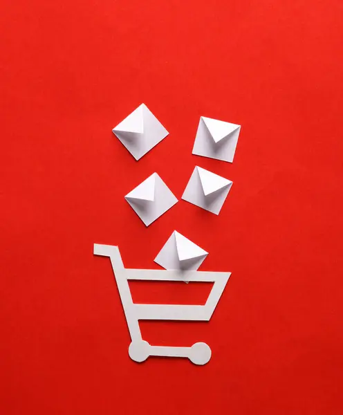 Paper cut shopping trolley with mail envelopes on red background