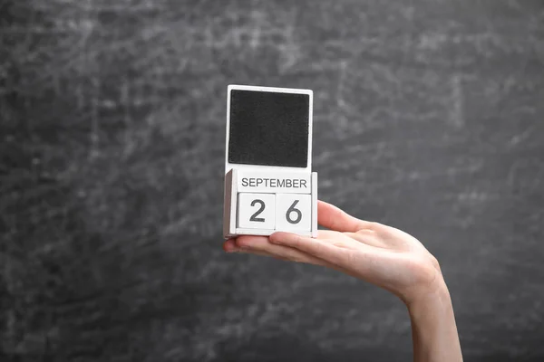 Wooden block calendar with date september 26 in female hand on background of school chalk blackboard