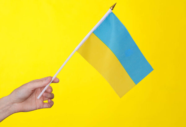 Woman's hand holds flag of Ukraine on a yellow background