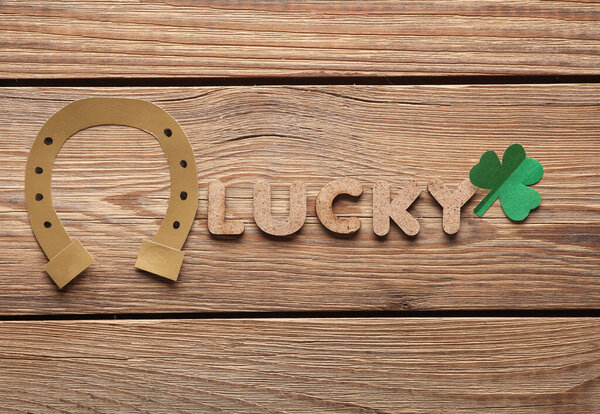 День Святого Патрика. Слово, счастливое с подковой и клевером, вырезанным из бумаги на деревянном столе. Плоский лежал