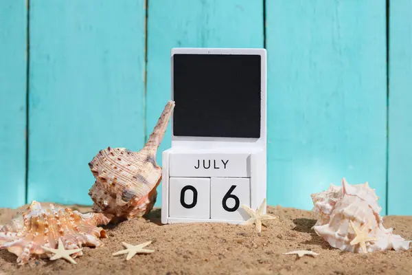 Beach holiday composition with sand, sea souvenirs and wooden block calendar with date july 06. Vacation, summertime, creative travel still life