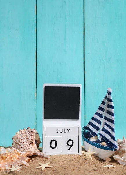 Beach holiday composition with sand, sailboat and wooden block calendar with date july 09 Vacation, summertime, creative travel still life