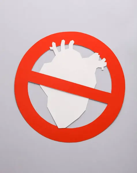 Paper-cut anatomical heart with a prohibition sign on a gray background. Prohibition of transpontology